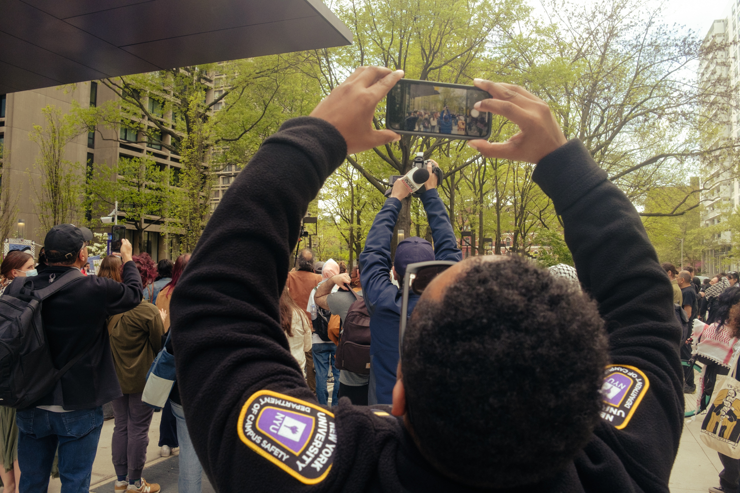 A Campus Safety officer takes a photo of a cameraman filming the encampment.