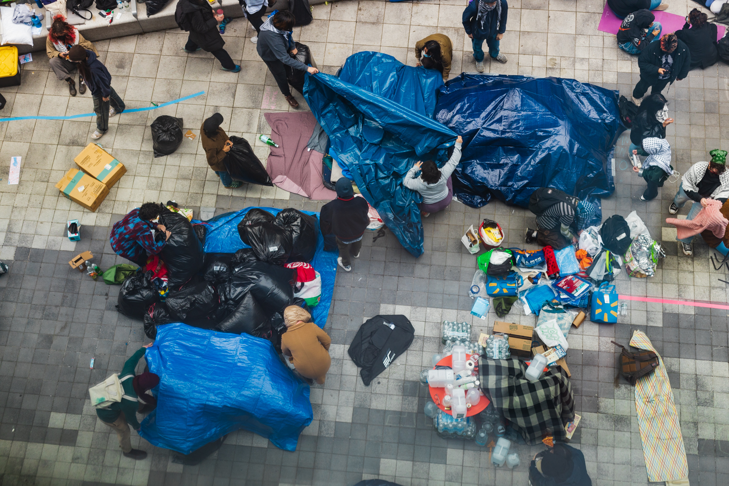 Aerial view of protestors putting up blue tarps over supplies inside the encampment.