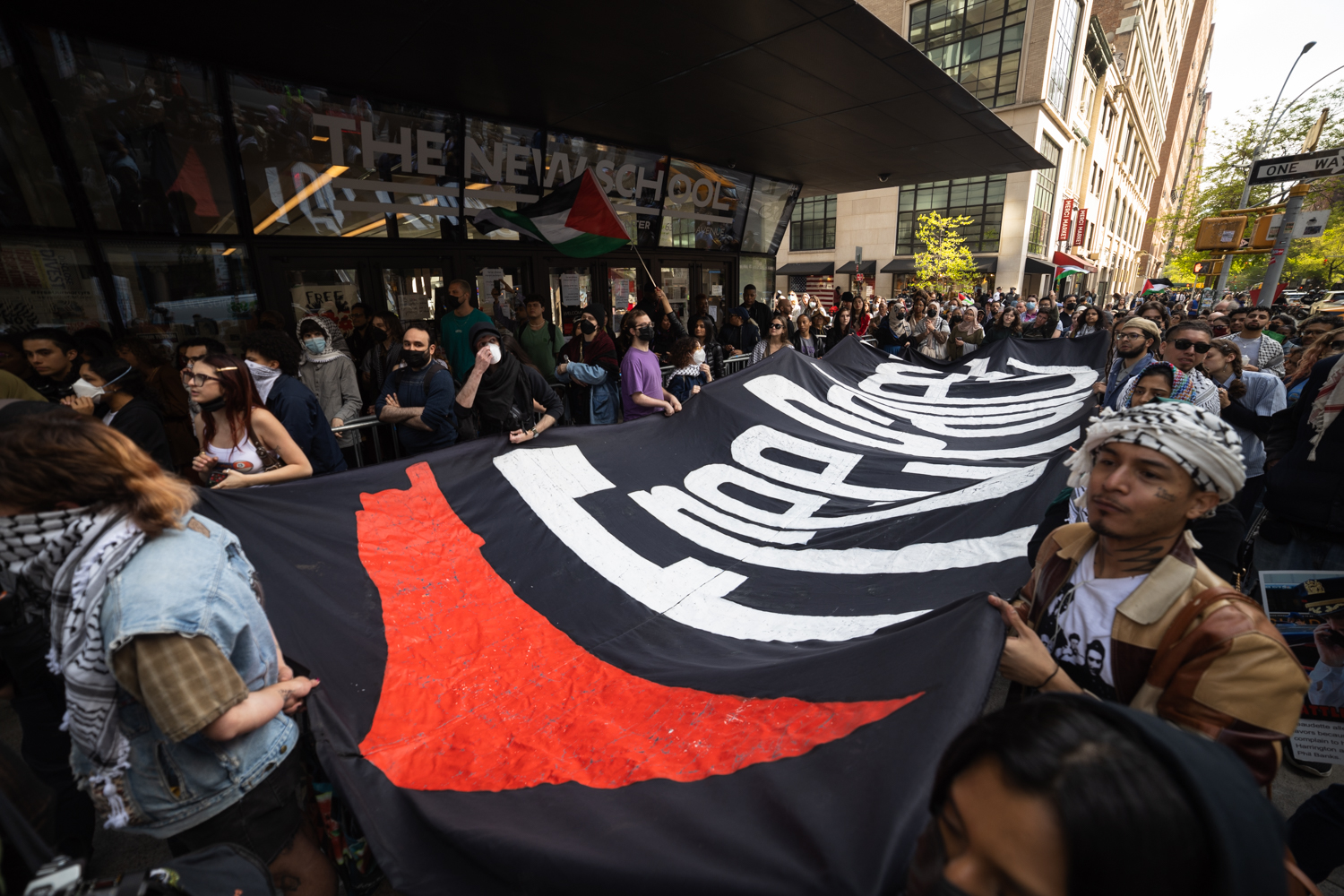 Protesters holding a black banner that reads “Free Palestine” outside The New School.
