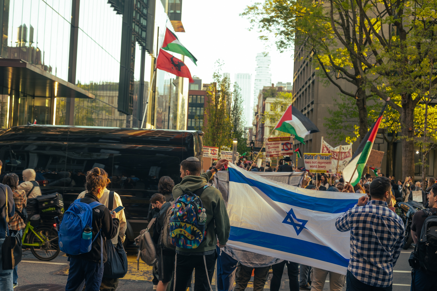 A group of pro-Israeli counterprotesters hold up an Israeli flag across the street from the encampment, where pro-Palestinian protesters are chanting.
