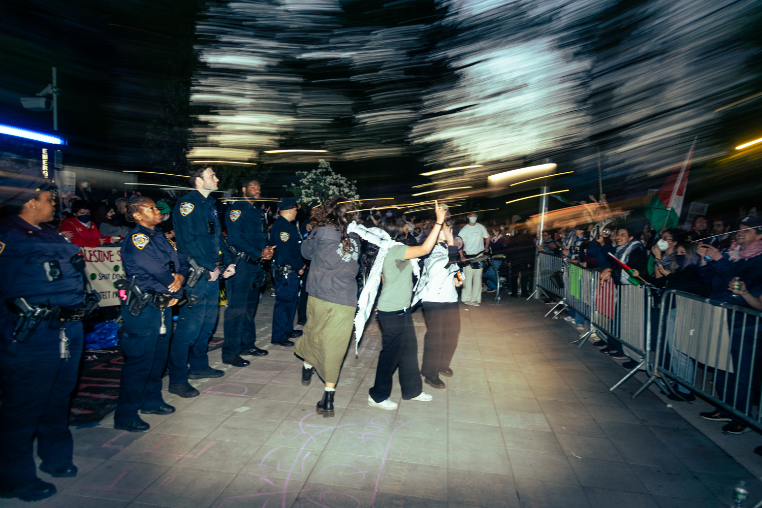 Protesters within the encampment lead chants and dances in front of a line of N.Y.P.D. officers.
