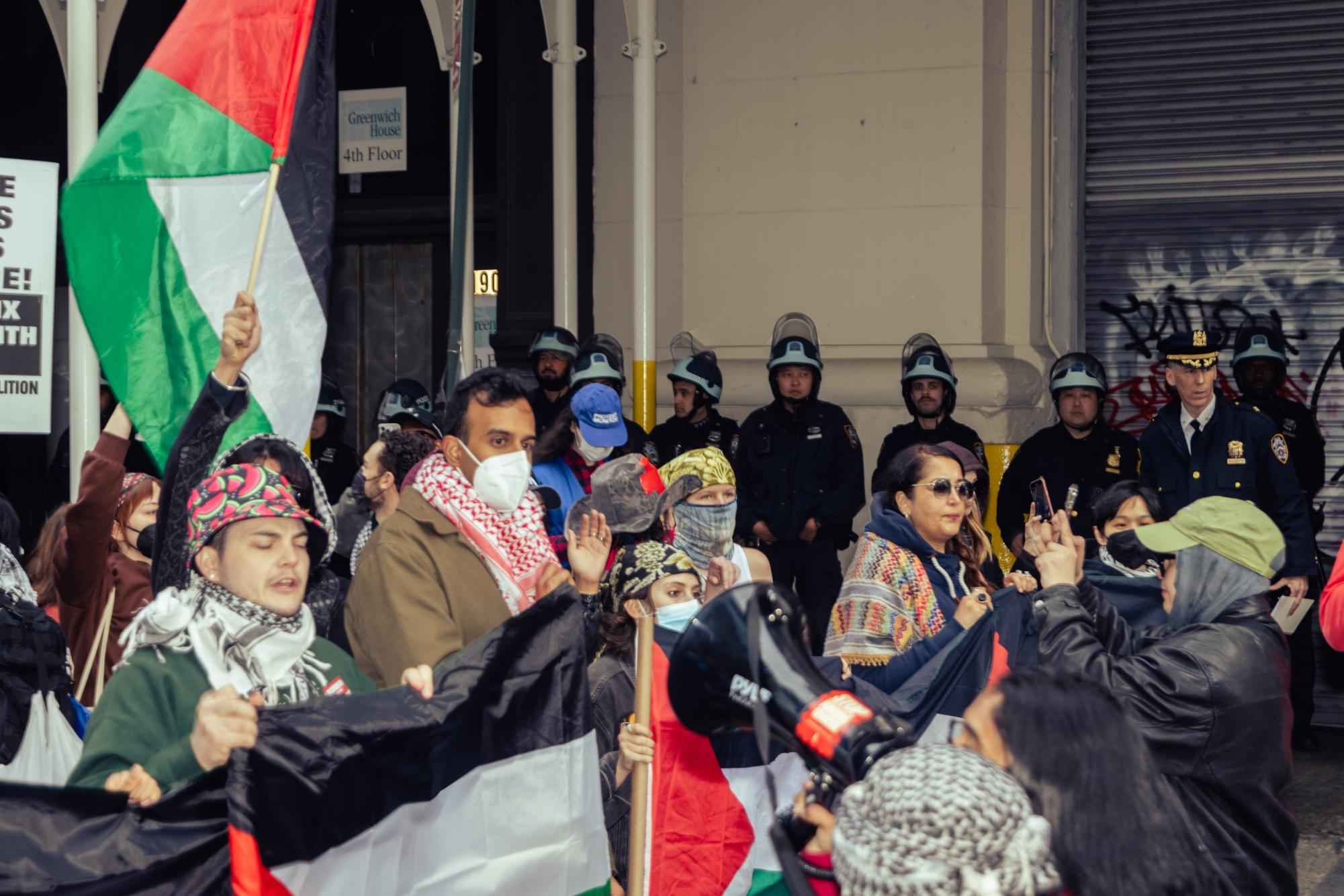 Pro-Palestinian protesters in a march in the foreground and police in riot gear in the background.