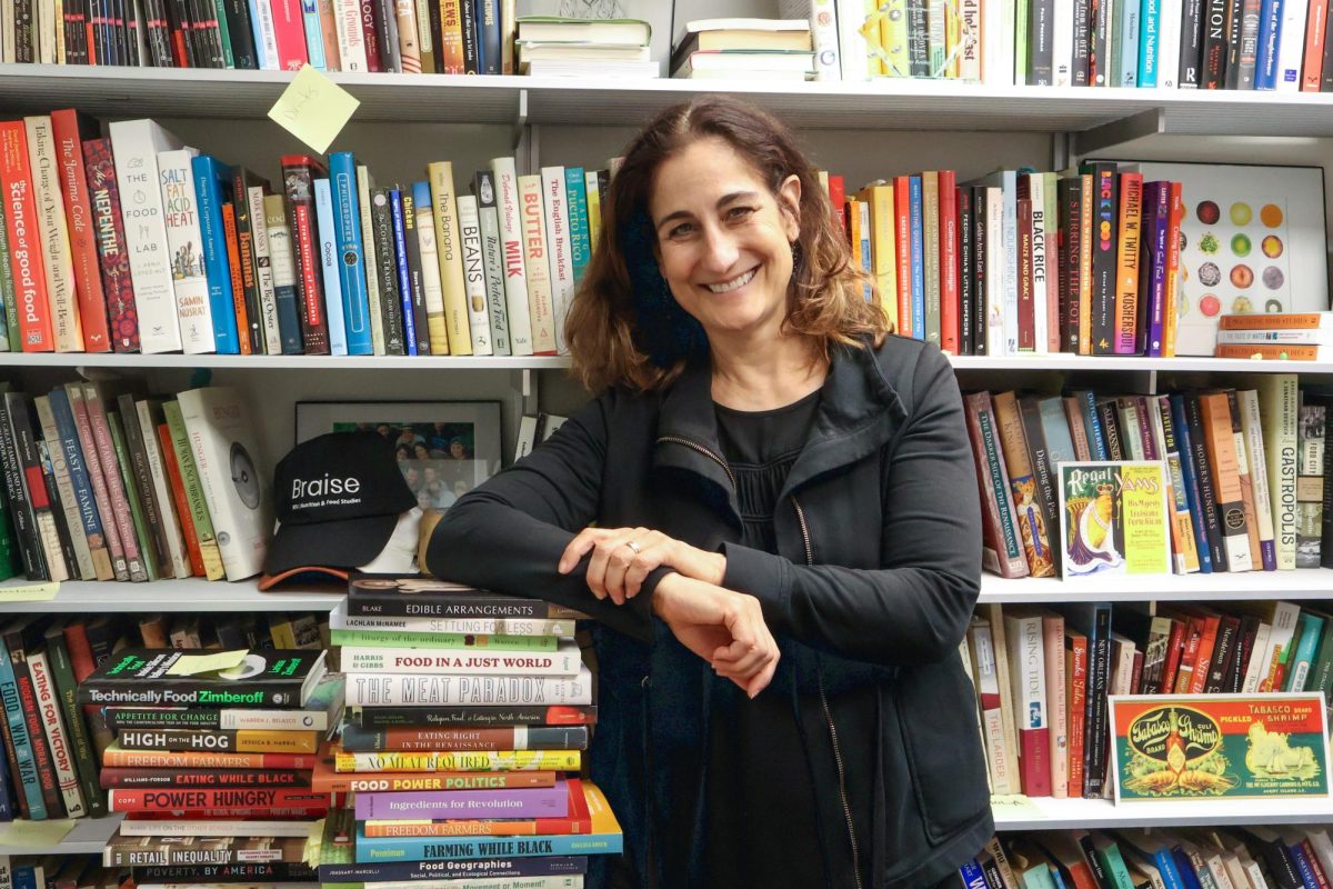 Woman posing by leaning on a stack of books while standing in front of a shelf packed with books.