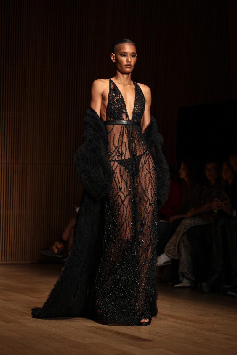 A model in a black, lace bodysuit with knee–length tassels hanging from the neckline.