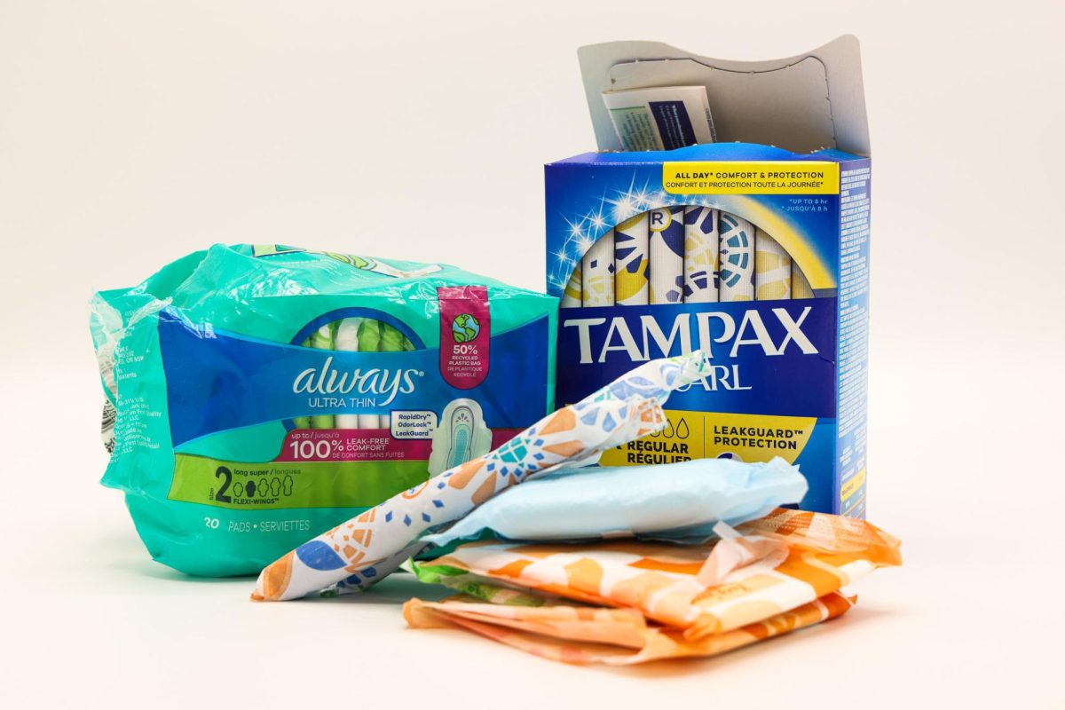 Packages of menstrual products, with individual pads and tampons piled in front of them.