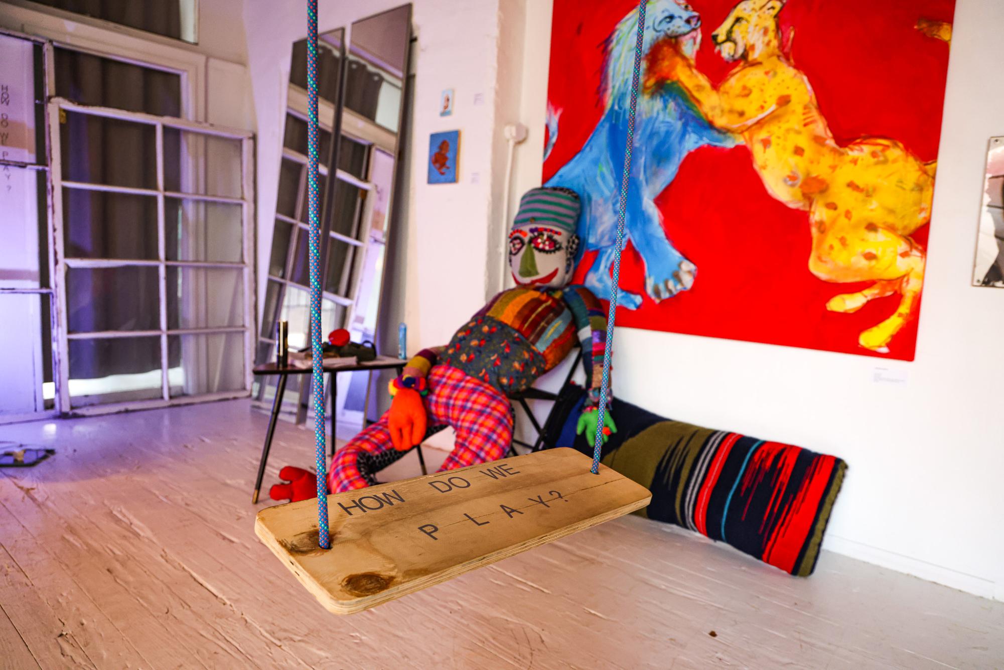 A white room with a stuffed dummy sitting on a black folding chair, a painting with a leopard lion fighting and a mirror in the background.