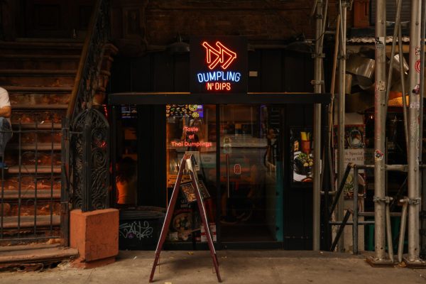 A storefront with “DUMPLING N’ DIPS” in red and blue, neon lettering and an A-frame sign in front of the steps.