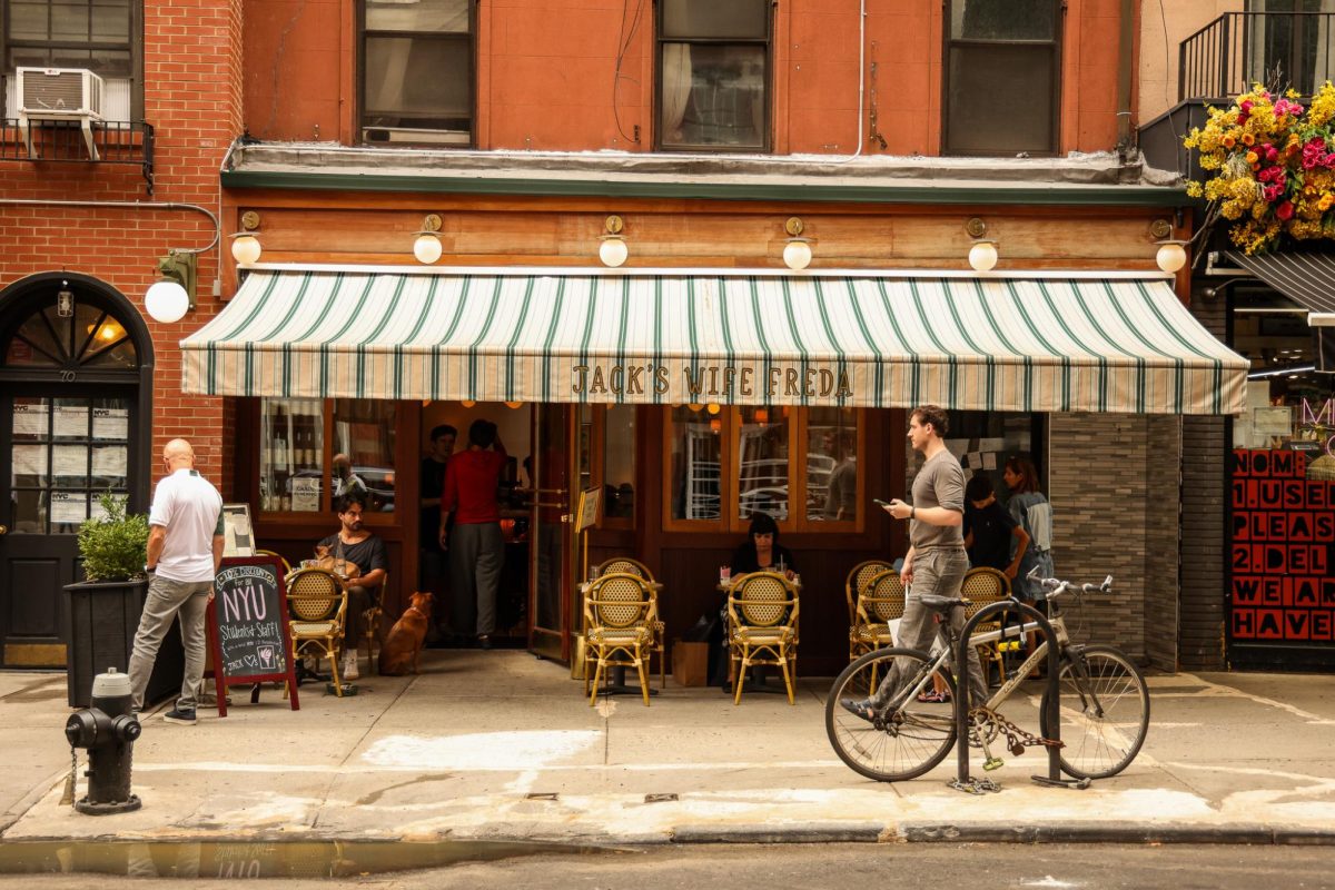 A weathered wooden storefront with “JACK’S WIFE FREDA” in gold text on a green and white striped awning hanging over small yellow tables and chairs.