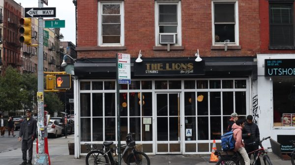 A storefront with a black awning that reads “THE LIONS ST.MARKS Bar and Grill” in a white and rustic gold font.