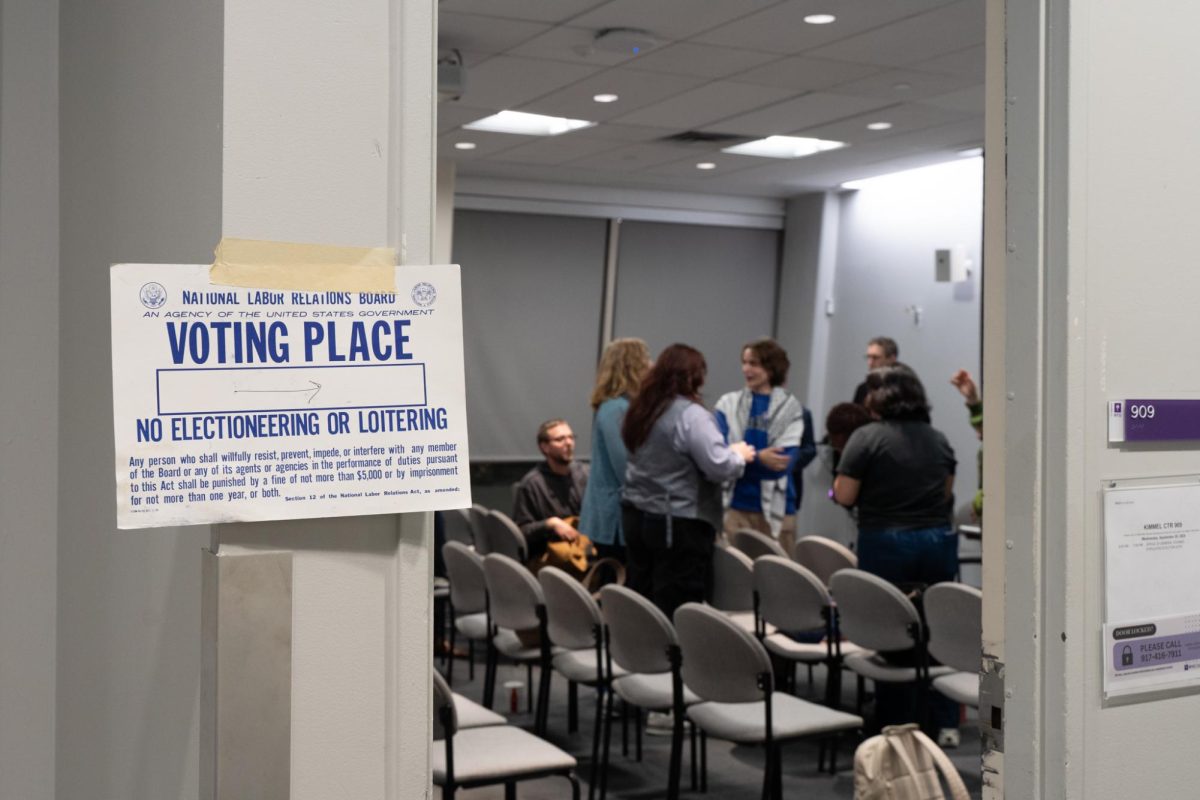 A flier with the words “VOTING PLACE” taped to a doorway with a group of people inside the room.