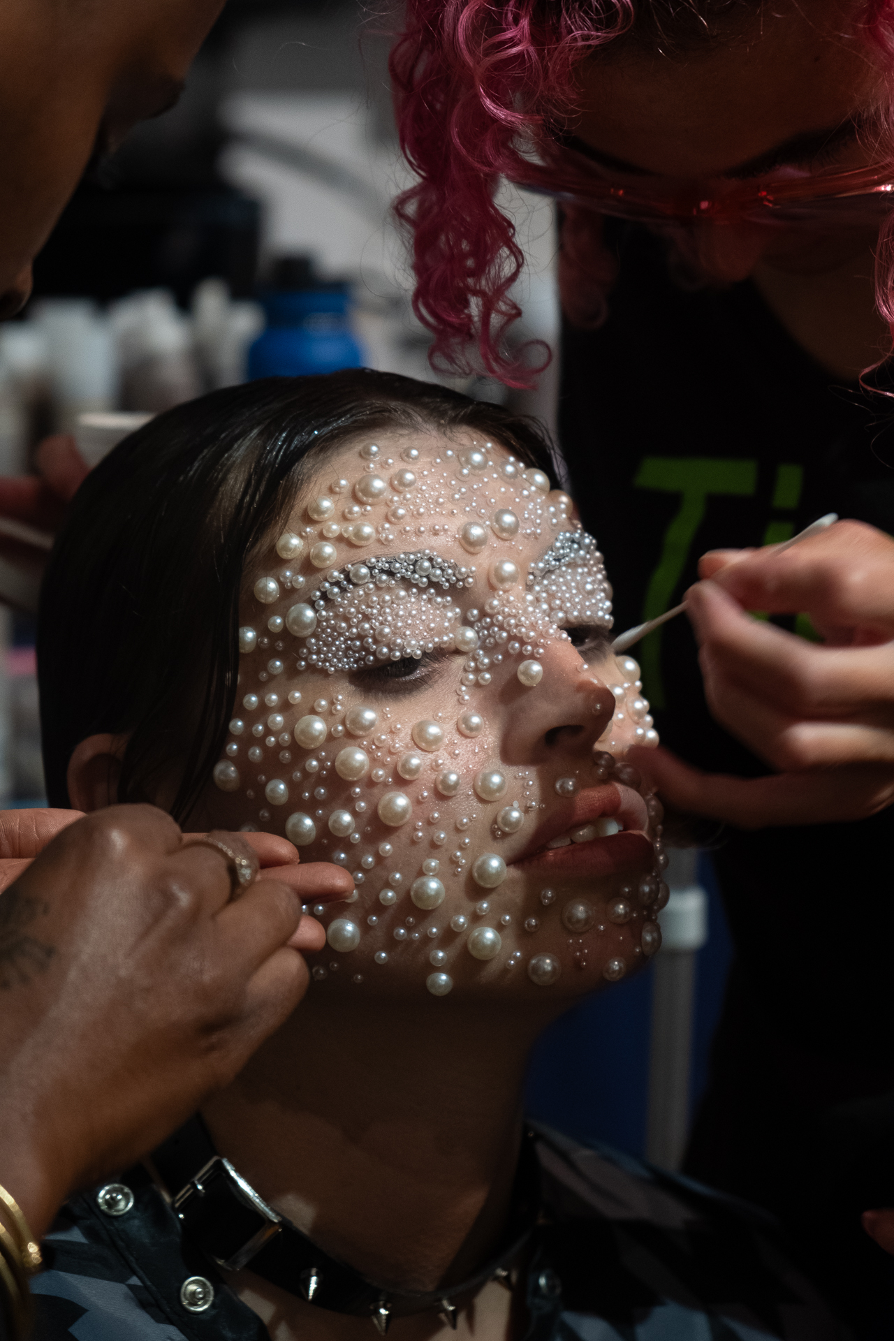 Several people glue pearls to a model’s face.