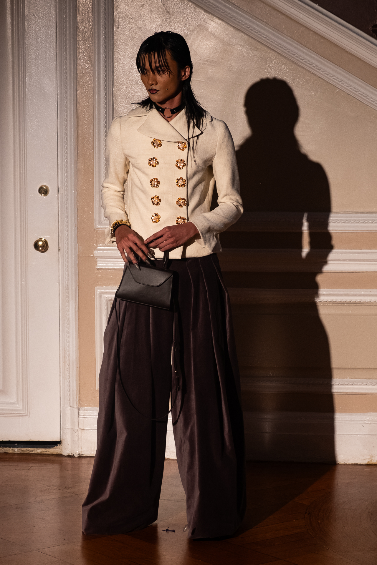 A model poses in black wide-leg pants and a white button up with gold flower details.