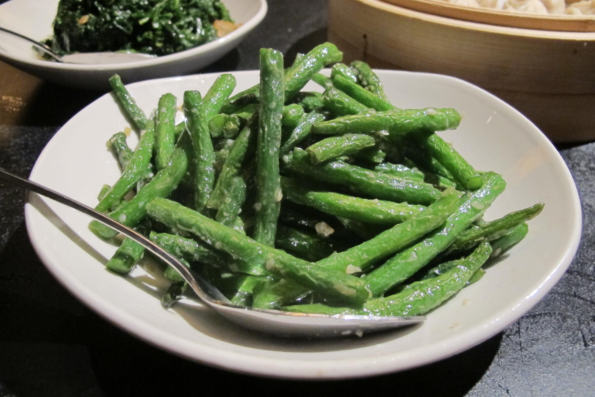 String beans sprinkled with garlic in a white bowl, with a metal spoon in the bowl.