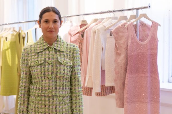 A model wears a pink and green tweed jacket in front of clothing racks.