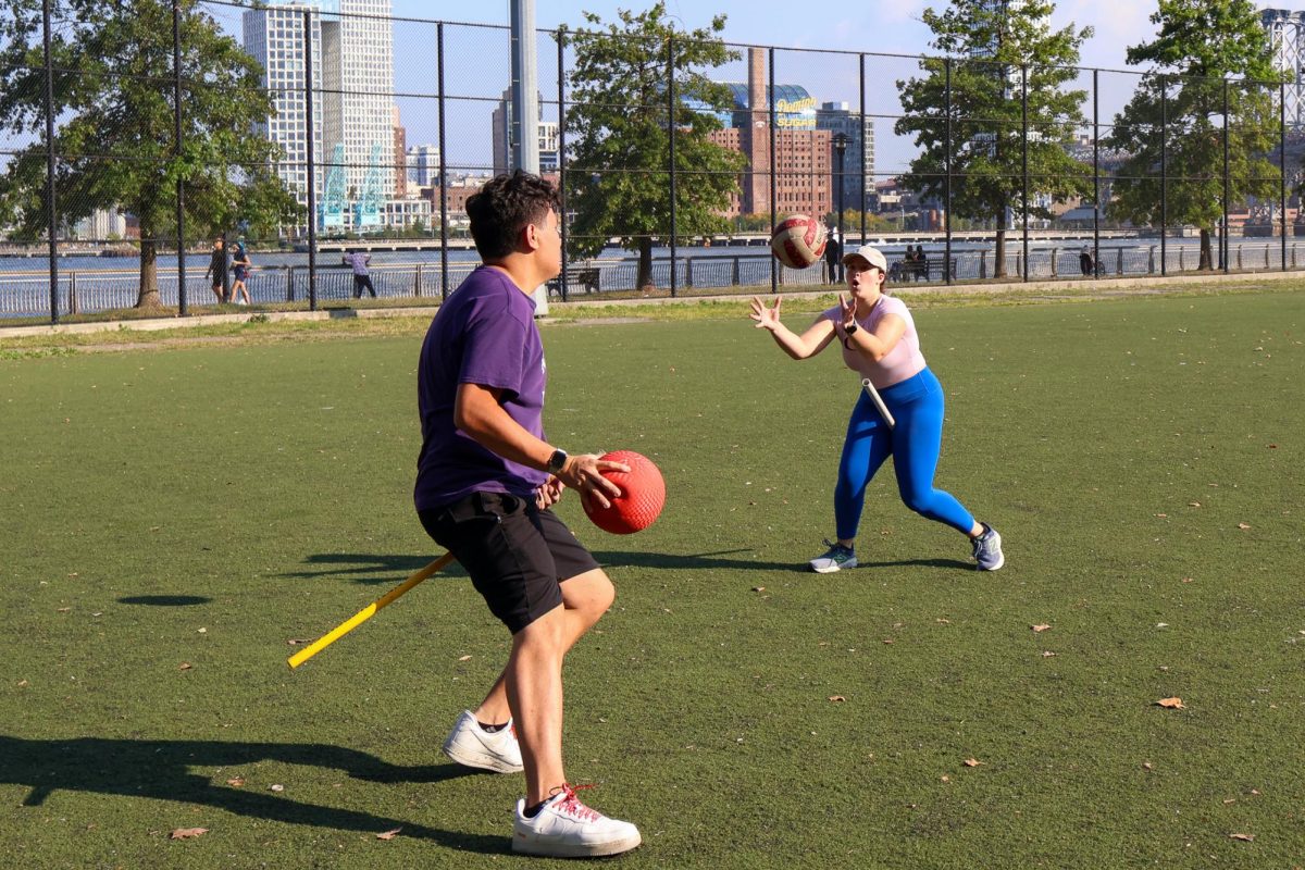 Quadball players on a field, with one player passing a volleyball to their teammate.