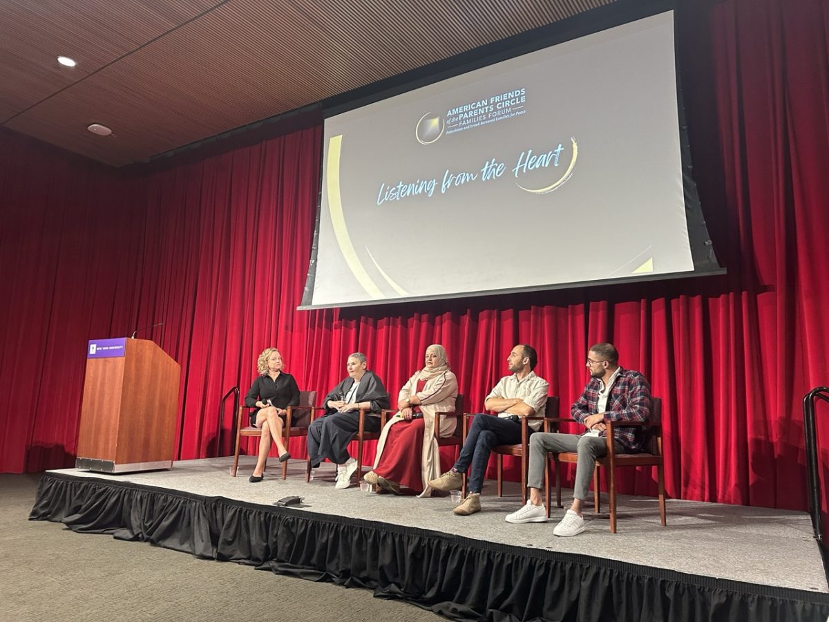 Five panelists sit on a stage in front of a red curtain and a screen that reads “Listening from the Heart”.