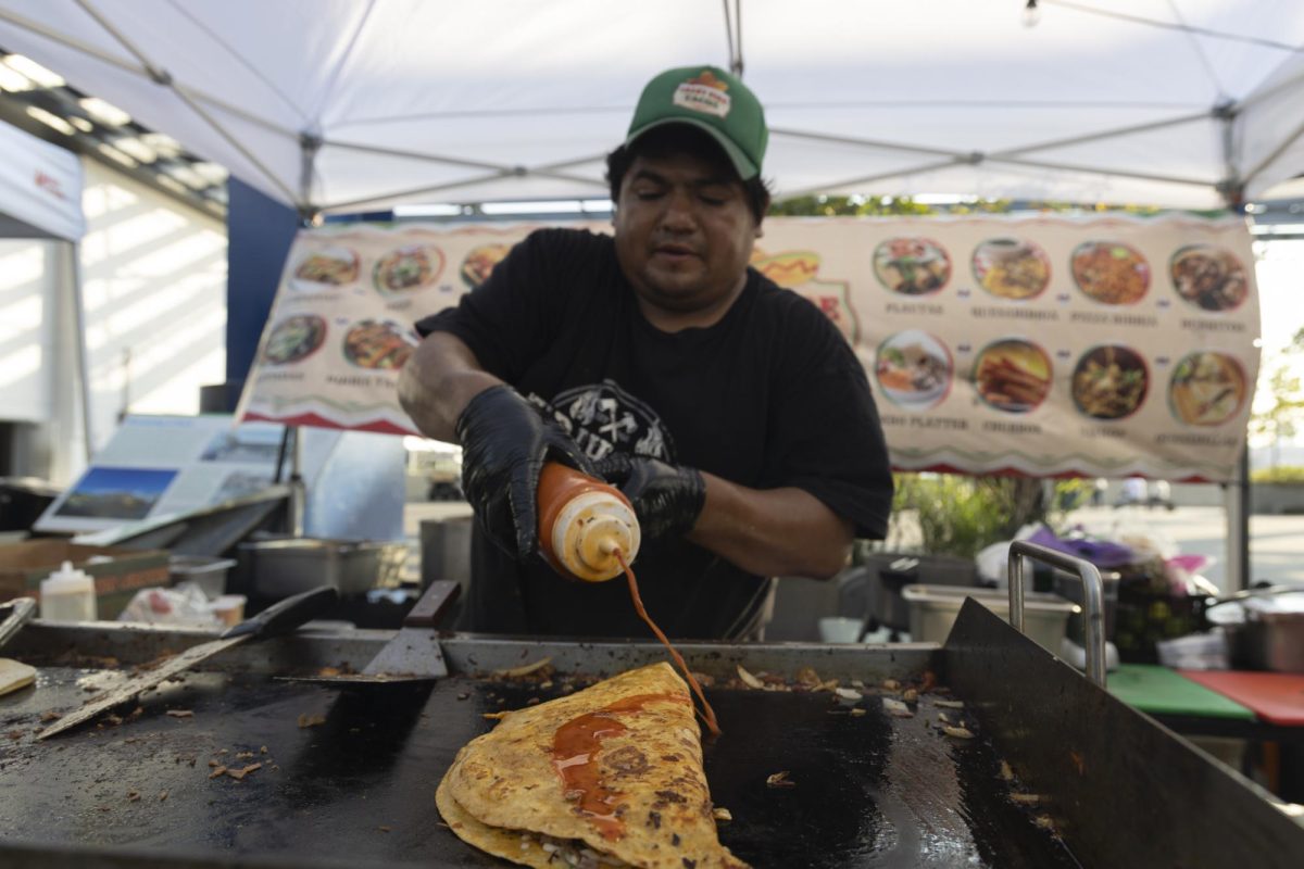 A man pouring orange sauce over a grill with a large folded tortilla on it.