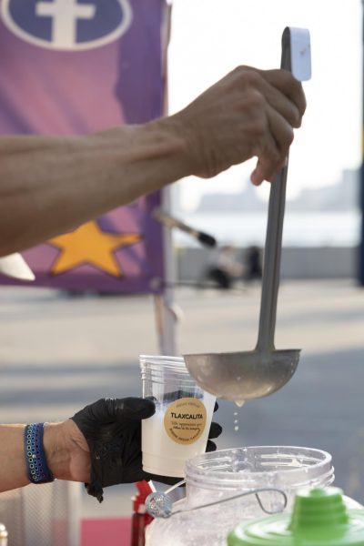 A ladle pouring white liquid into a clear cup that says “TLAXCALITA” on it.