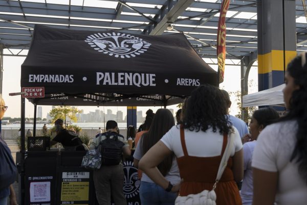 People in line for a black tent that reads “EMPANADAS”, “PALENQUE” and “AREPAS” on it in white.