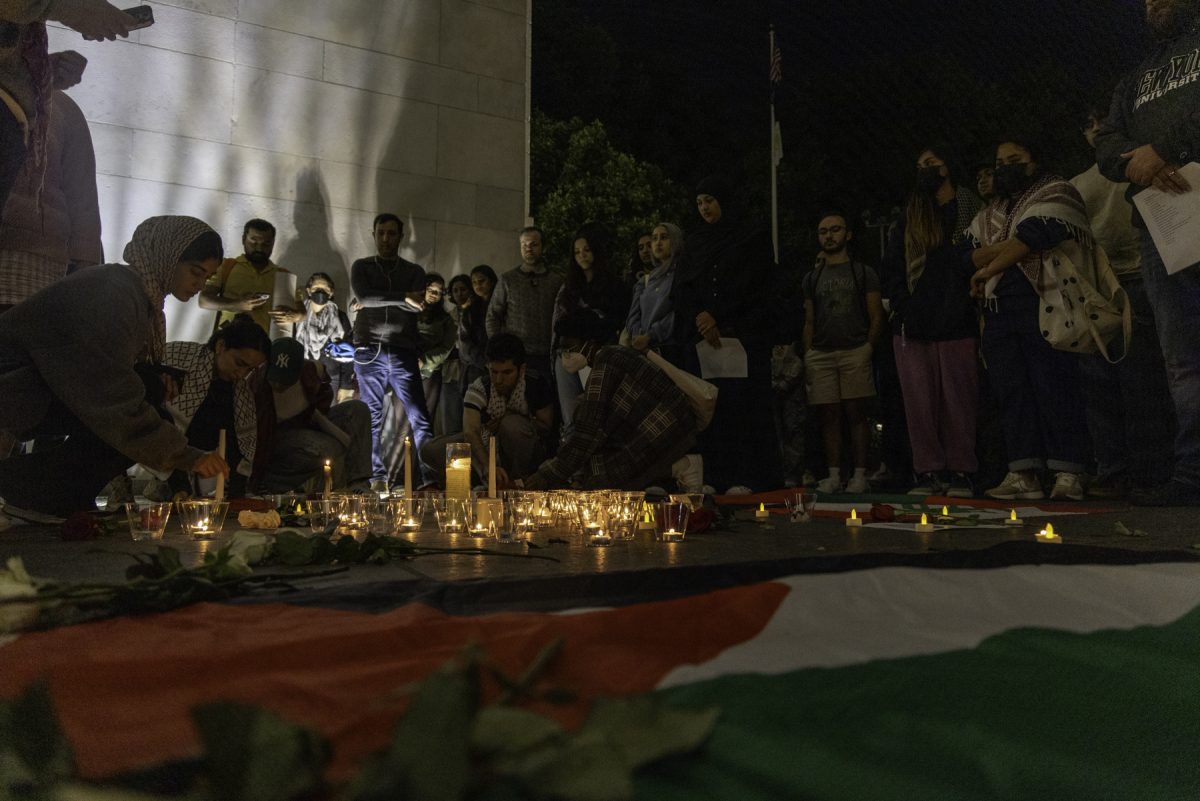 People in multi-colored outfits stand in a circle around candles and flags on the ground.