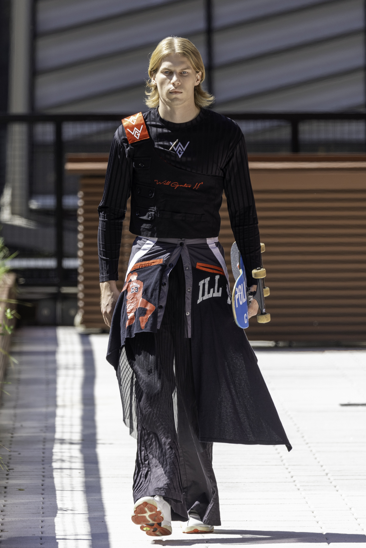 A model wearing a glossy black puffer, white crop top, black glossy pants and white shoes holding a yellow handbag walks down the white tiled runway.