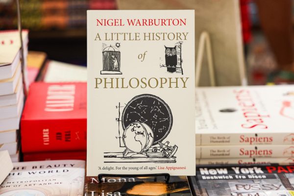 A book with a white cover with drawings of an owl, a person in the rain with an umbrella and a globe in front of a constellation map. “A LITTLE HISTORY OF PHILOSOPHY” is written in gold on the front.