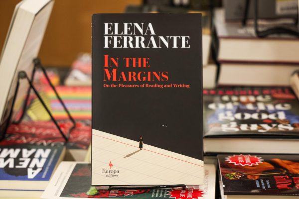 A black book with “ELENA FERRANTE” written on the top in white and “IN THE MARGINS” written in the middle in red. The book is on a book stand.