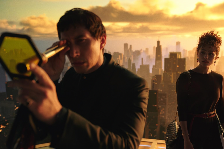 Two people stand against a cityscape, one of them looks through a scope.