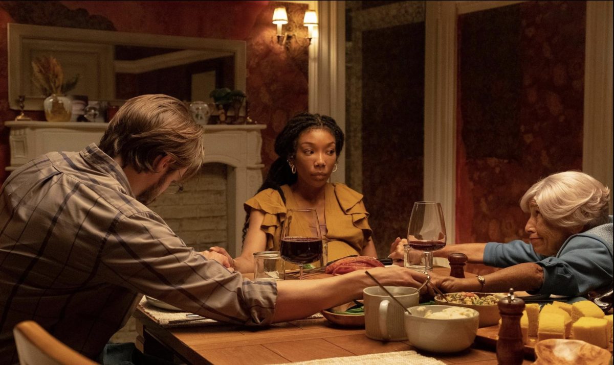 A man and two women sit around a table, all holding hands in a candlelit room with red walls and food on the table.