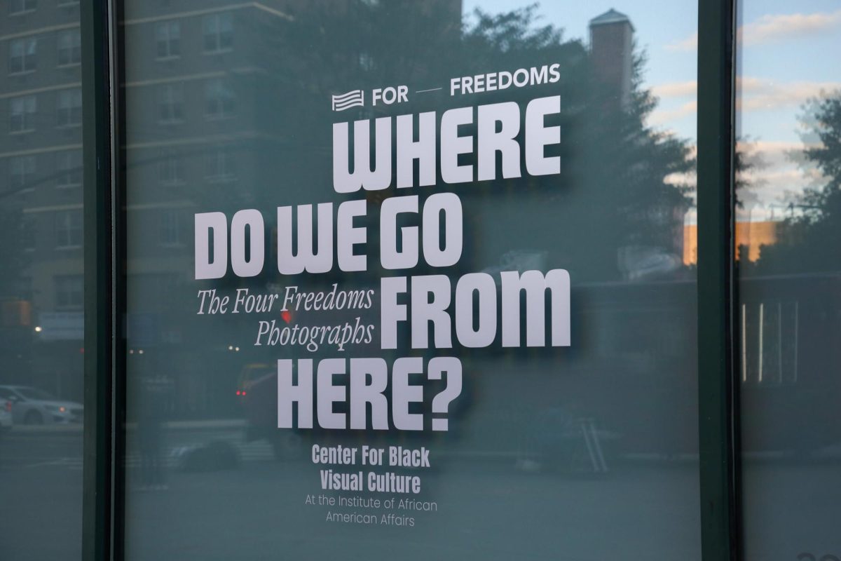 A window pane with signage for an art exhibit reads "Where Do We Go From Here? The Four Freedoms Photographs."