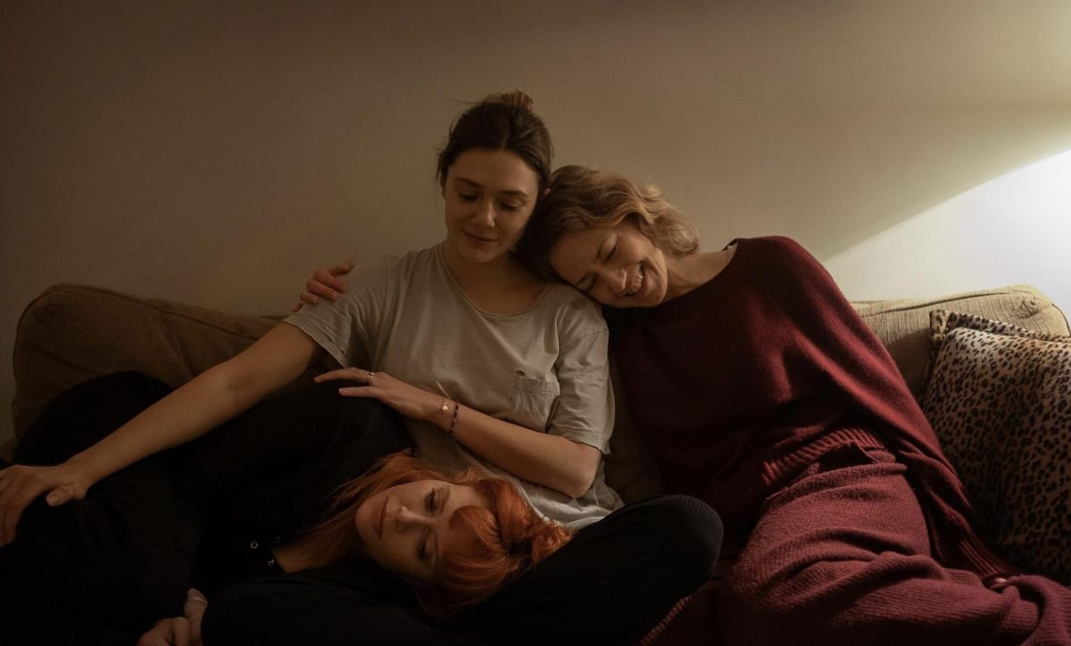 Three women on a couch lean on each other.