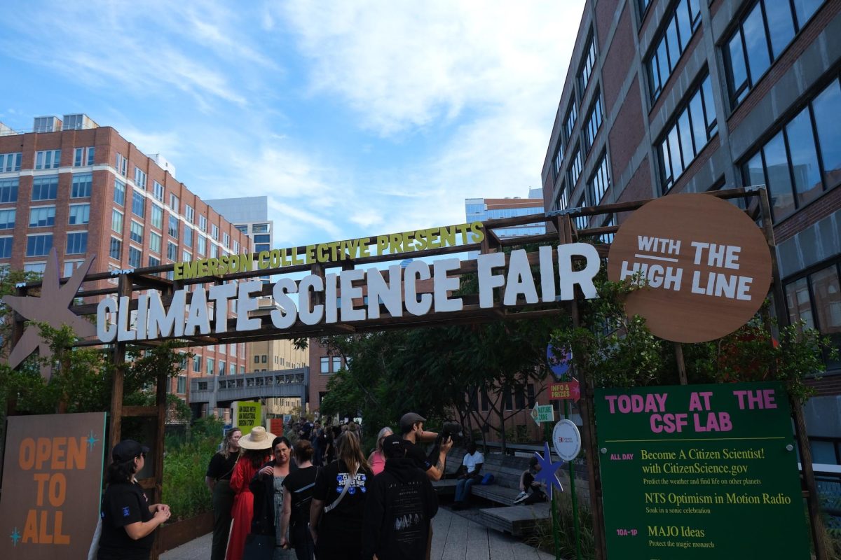 Between buildings is a small park with a colorful sign in front of a path with the words “EMERSON COLLECTIVE PRESENTS CLIMATE SCIENCE FAIR WITH THE HIGH LINE.”