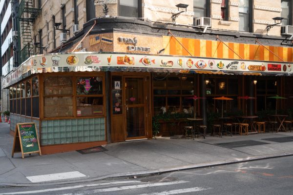 A storefront with the words “THAÍ DINER” has bistro tables, chairs, and mounted umbrellas out front.