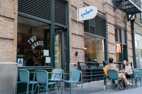 A storefront with the words “two hands” written on the window. There are wooden tables and blue chairs out front.