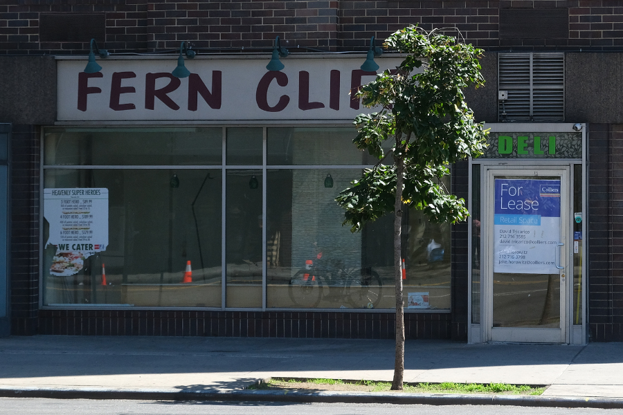 A closed deli with sticker advertisements peeling off its windows and a “For Lease” sign on the front.