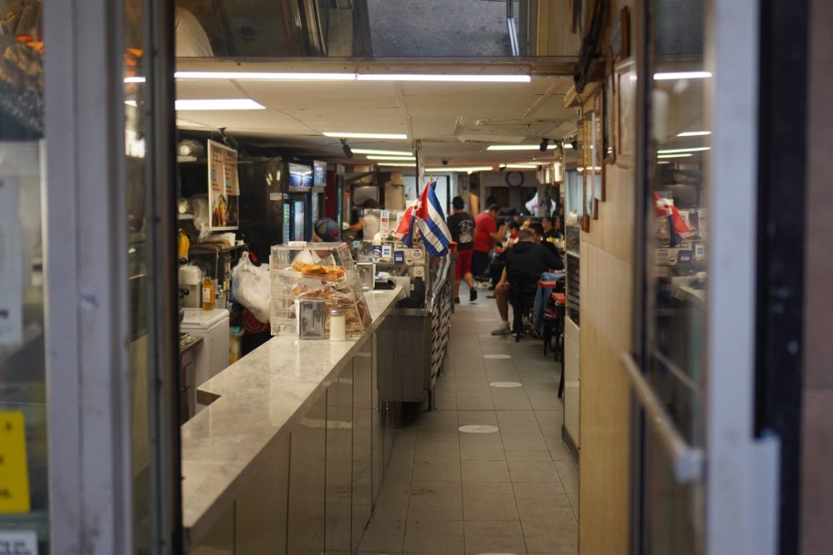 A look inside a Cuban restaurant. Pictured are tables and chairs against the walls and employees behind the counter.