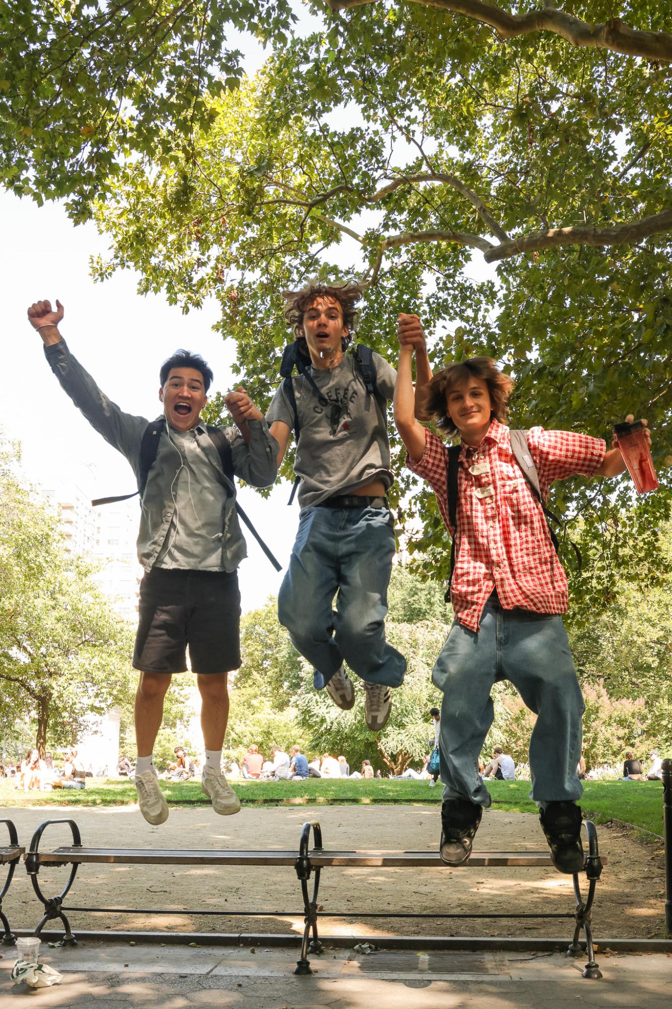 Three people hold hands while jumping off of a park bench.