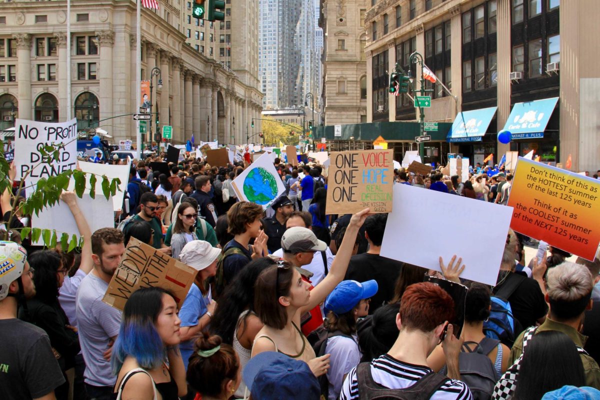 Protestors walk through a crowd, holding various signs in favor of climate change reform, one reads “ONE VOICE, ONE HOPE, ONE REAL DECISION”.