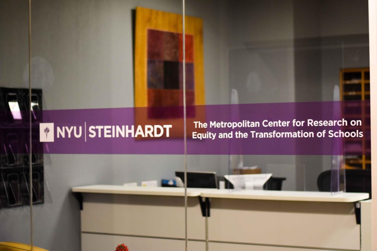 On a glass wall in front of an office front desk is a purple stripe with the words “N.Y.U. STEINHARDT” and “The Metropolitan Center for Research on Equity and the Transformation of Schools” written on it.