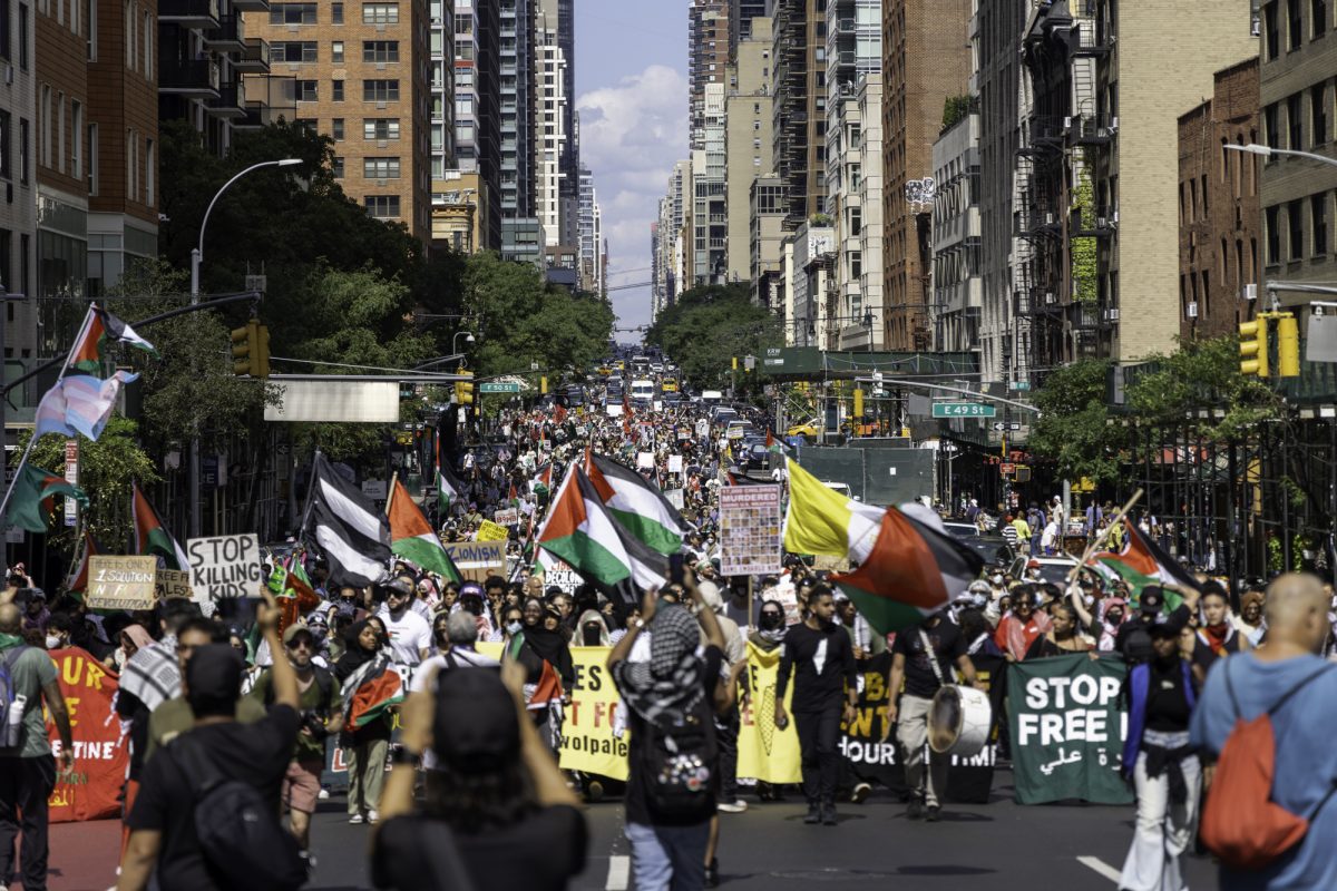 Hundreds of protesters march down a road with signs and Palestinian flags.