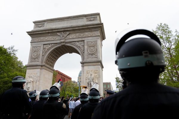 The photo is shot from behind a troupe of police in helmets surveying a group of protesters while the Washington Square Arch stands above them all.