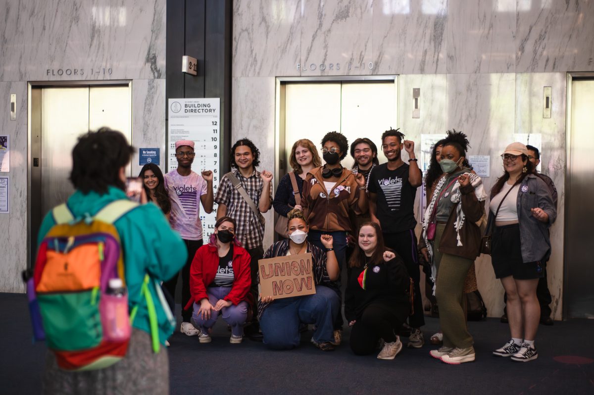 A group of people posing for a picture. The person in the middle is holding a sign that says “UNION NOW.”