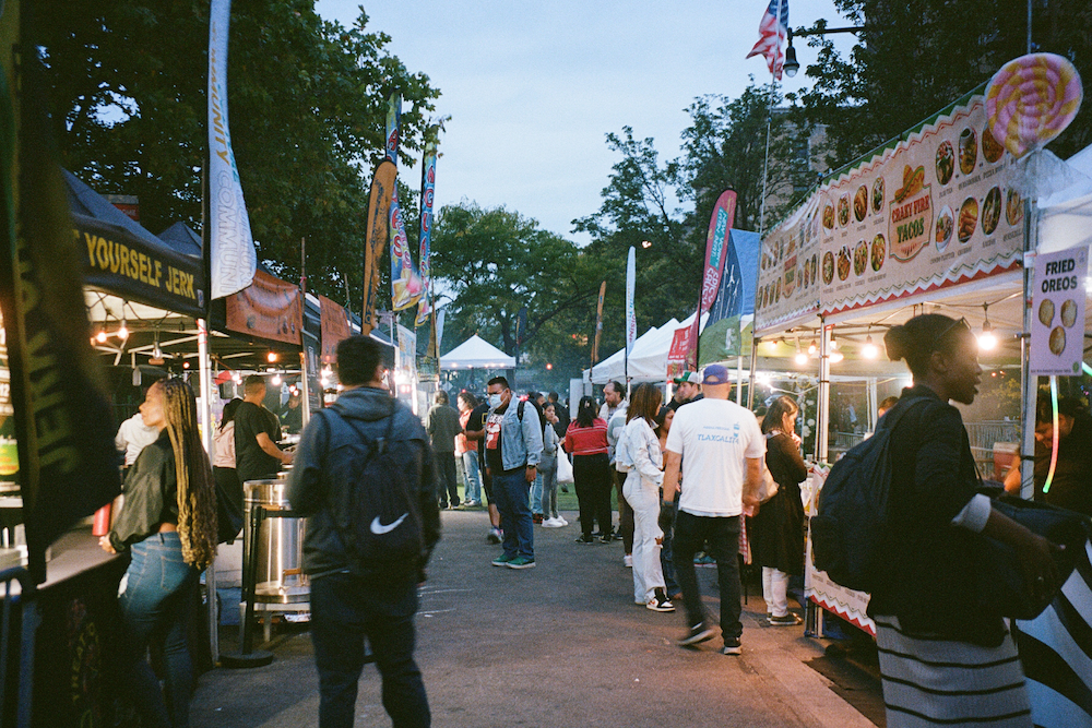 A street of food vendors and people walking and waiting in line.