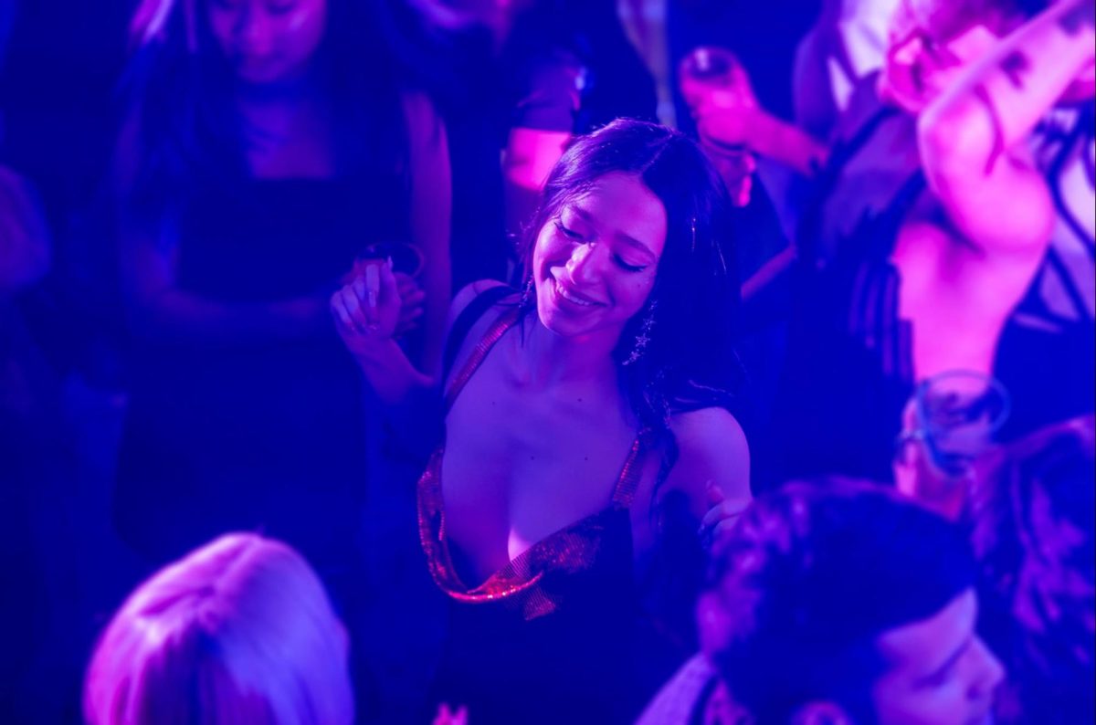 A girl in a red glitter dress dancing under purple lighting in a club.