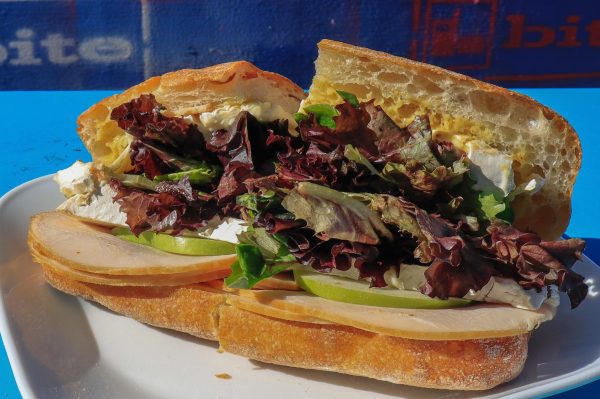 Closeup of a French Bite sandwich filled with apple slices, lettuce, turkey, brie cheese and mustard sitting on a blue table.