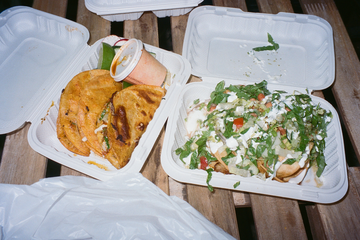 Two white to-go boxes next to each other, one with tacos and one with a salad.