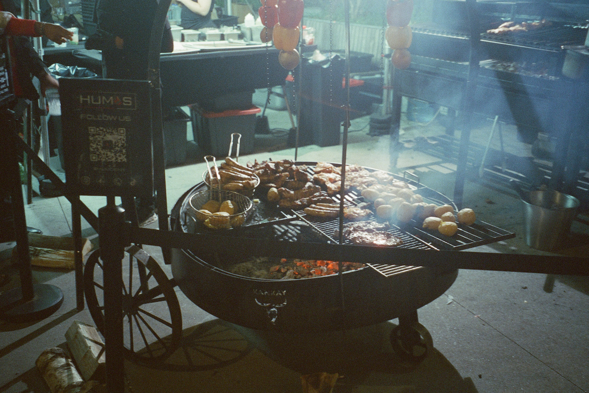 A grill on wheels with potatoes and meat on it, burning above coal.