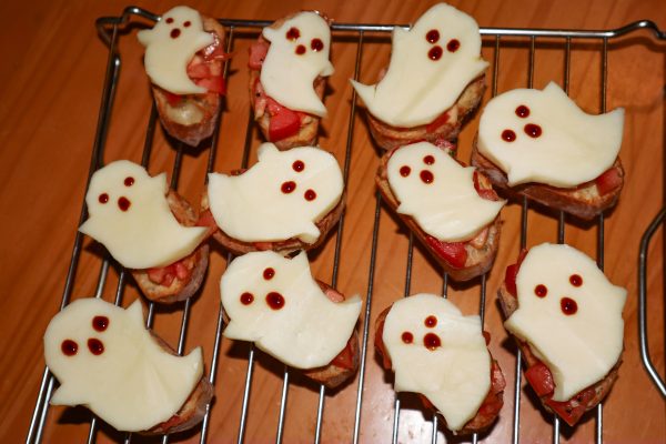 Eleven breads with a tomato and a ghost-shaped cheese on top.