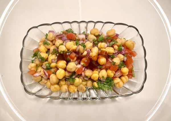  A glass dish of chickpea salad that includes corn, tomatoes, cilantro, red onions and a drizzle of sauce.