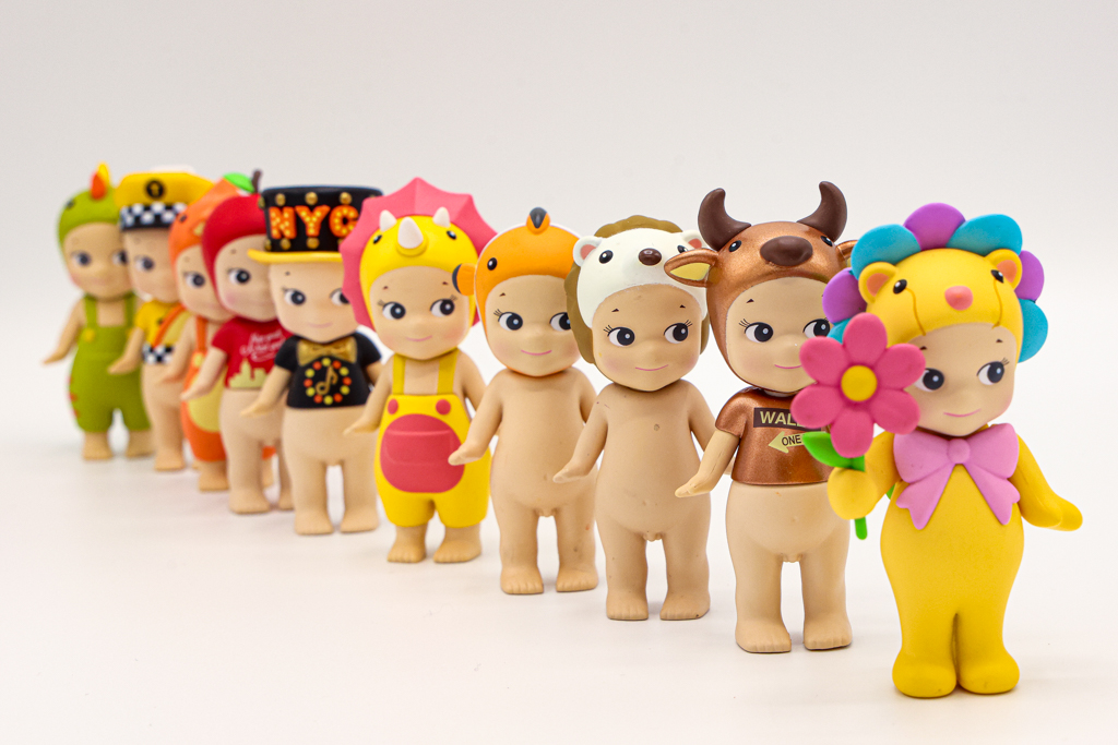 A photo of toy angels in a line, wearing various bright hats and outfits.